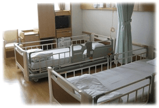 二人部屋のようす。介助用の柵付きベッドが2床並び、間仕切りのカーテンと収納を備えた病室