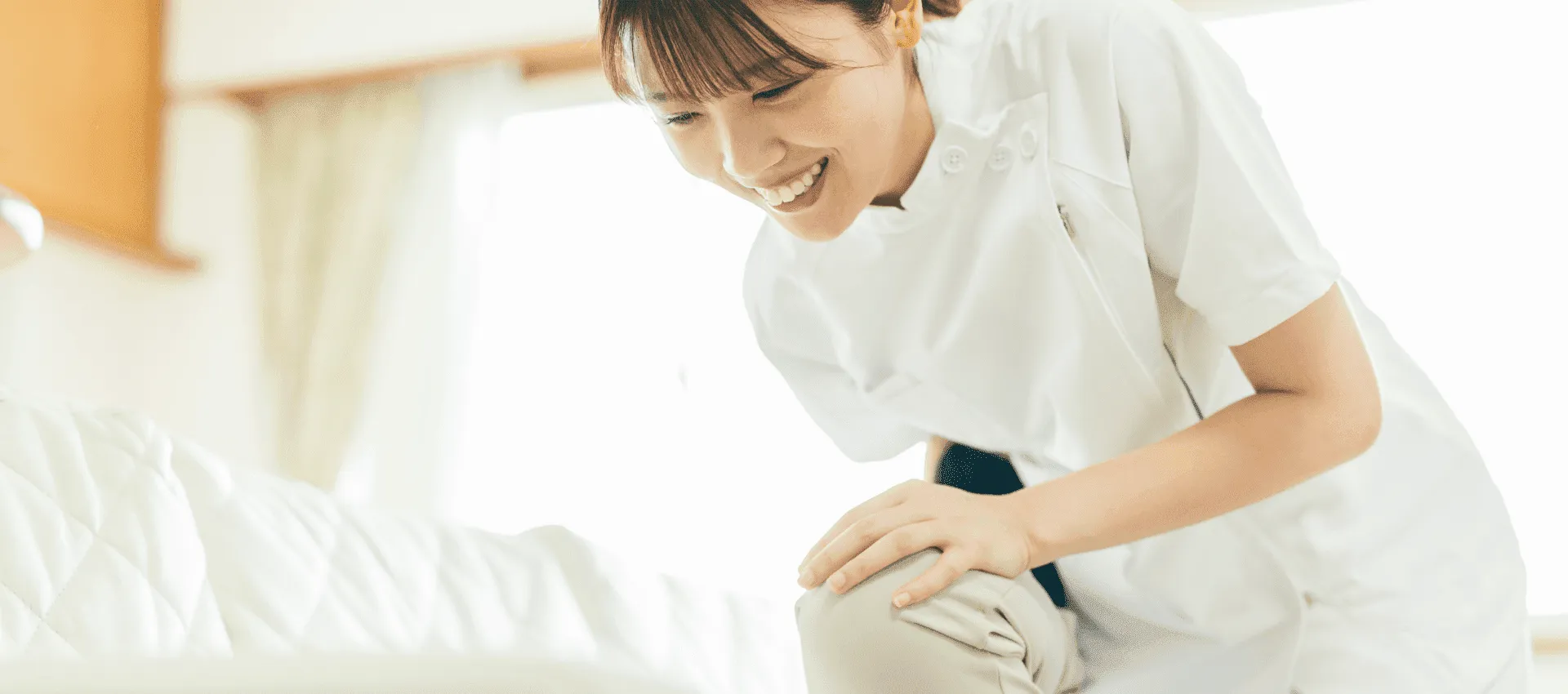 病室でベッドサイドにかがみ、笑顔で患者さんに話しかける看護師